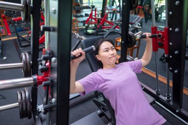 Çinli Doğu Asyalı kadın spor salonunda göğüs pres makinesi eğitimi alıyor. Spor salonu ve sağlıklı yaşam tarzı konsepti