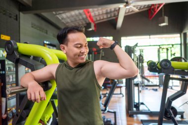 Endonezyalı güneydoğu Asyalı adam spor salonundaki eğitimden sonra kol kaslarını gösteriyor. Spor salonu ve sağlıklı yaşam tarzı konsepti