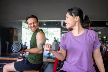 Endonezyalı güneydoğu Asyalı erkek ve Çinli Asyalı kadın spor salonunda dambıl kaldırıyor. Spor salonu ve sağlıklı yaşam tarzı konsepti