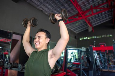Endonezyalı güneydoğu Asyalı adam spor salonunda dambıl kaldırırken spor yapıyor. Spor salonu ve sağlıklı yaşam tarzı konsepti