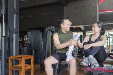 Endonezyalı Güneydoğu Asyalı özel antrenör spor salonundaki Çinli Doğu Asyalı kadına plastik şişe veriyor. Spor salonu ve sağlıklı yaşam tarzı konsepti