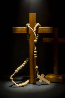 Tahta Hıristiyan haçı ve koyu arkaplanda tespih. Işık etkisi. Dinin ve Tanrı 'ya ibadet etmenin sembolü. Umut, inanç ve din kavramı