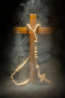 Tahta Hıristiyan haçı ve koyu arkaplanda tespih. Işık ve duman veya sis etkisi. Dinin ve Tanrı 'ya ibadet etmenin sembolü. Umut, inanç ve din kavramı