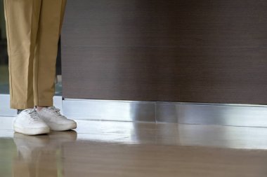 Modern ofis binasında ahşap zemini olan şık kahverengi pantolonlu ve beyaz ayakkabılı bir iş adamı bacağı. İş konsepti