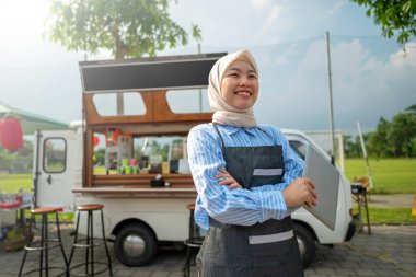 Endonezyalı güneydoğu Asyalı tesettürlü, tesettürlü Müslüman kadın barista kafesinin önünde tablet tutarken ayakta duruyordu. Kamyon üzerinde küçük bir kafe ya da kafe işletmesi