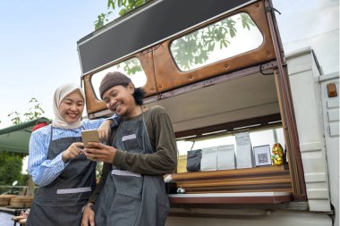 Endonezyalı güneydoğu Asyalı erkek ve kafeteryalarının önünde cep telefonu kullanan tesettürlü Çinli müslüman bir kadın. Kamyon üzerinde küçük bir kafe ya da kafe işletmesi