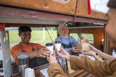 Endonezyalı güneydoğu Asyalı erkek ve tesettürlü Çinli Müslüman kadın müşterilere içki ve atıştırmalık servisi yapıyorlar. Kamyon üzerinde küçük bir kafe ya da kafe işletmesi
