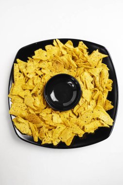 Siyah tabakta Nachos tortilla cipsi ve beyaz arka planda sos için boş bir kâse. Yiyecek ve atıştırmalık konsepti