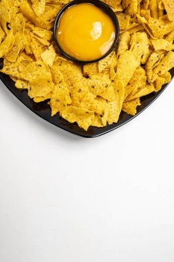Siyah tabakta Nachos tortilla cipsi ve beyaz arka planda peynir sosu. Uzayı kopyala Yiyecek ve atıştırmalık konsepti