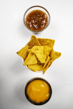 Peynirli nachos tortilla cipsi ve beyaz arka planda salsa barbekü sosu. Yiyecek ve atıştırmalık konsepti