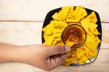 İnsan eli, salsa sosuna cipsli tortilla sosunu masanın üzerindeki kaseye batırıyor. Yiyecek ve atıştırmalık konsepti