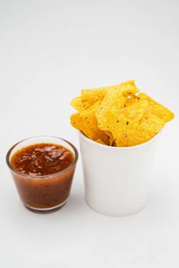 Beyaz arka planda cam bir kasede salsa soslu nachos tortilla cipsi. Yiyecek ve atıştırmalık konsepti