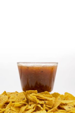 Beyaz arka planda cam bir kasede salsa soslu nachos tortilla cipsi. Yiyecek ve atıştırmalık konsepti