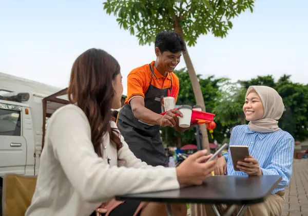Endonezyalı güneydoğu Asyalı erkek barista müşteriye içki ve yemek servisi yapıyor. Kamyon üzerinde küçük bir kafe ya da kafe işletmesi
