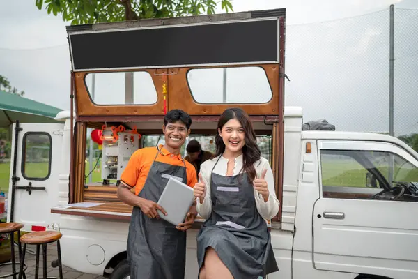 Endonezyalı güneydoğu Asyalı çift baristalar tableti kafelerinin önünde tutarken kendilerine güveniyorlar. Kamyon üzerinde küçük bir kafe ya da kafe işletmesi