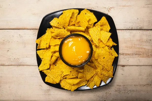 Masadaki peynir soslu siyah tabakta Nachos tortilla cipsi. Yiyecek ve atıştırmalık konsepti
