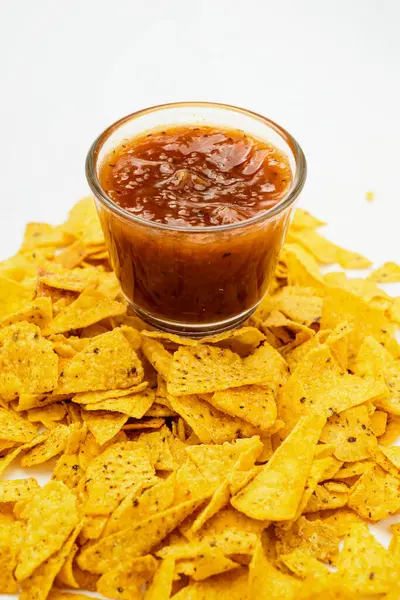 Beyaz arka planda cam bir kasede salsa soslu nachos tortilla cipsi. Yiyecek ve atıştırmalık konsepti