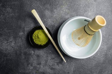 Siyah kasede kibrit yeşili çay tozu, tahta bir kaşık ve siyah bir masada boş bir kasede geleneksel bambu fırçası çırpma. Uyuşan yeşil çay yapmak için aksesuarlar. Üst görünüm