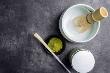 Siyah kasede kibrit yeşili çay tozu, tahta bir kaşık ve siyah bir masada boş bir kasede geleneksel bambu fırçası çırpma. Uyuşan yeşil çay yapmak için aksesuarlar. Üst görünüm