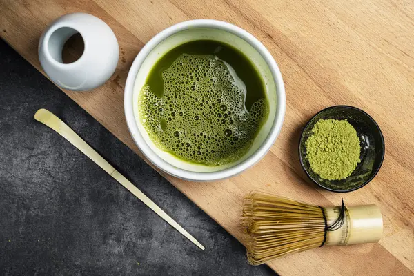 Siyah kasede kibrit yeşil çay tozu ve masada kaşık olan geleneksel bambu fırçası çırpıcısı. Uyuşan yeşil çay yapmak için aksesuarlar. Üst görünüm