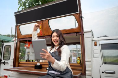 Endonezyalı güneydoğu Asyalı bayan barista elinde tabletle kafesinin önünde heyecanlı bir ifadeyle duruyordu. Kamyon üzerinde küçük bir kafe ya da kafe işletmesi