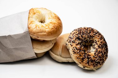 Beyaz arkaplanda izole edilmiş kahverengi kağıt torbadan muhtelif türde simit ekmekleri koleksiyonunun yakın görüntüsü