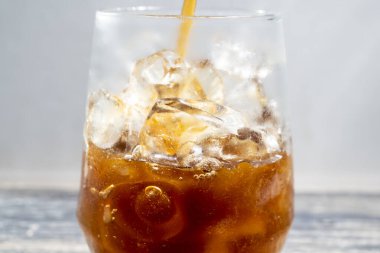 Yakın çekim, masada buz küpleri olan bir bardağa dökülen demlenmiş kahvenin görüntüsü.