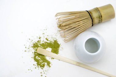 Geleneksel bambu çırpısı, kaşık ve beyaz arka plana serpilmiş yeşil çay tozu. Uyuşan yeşil çay yapmak için aksesuarlar. Üst görünüm