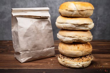 Muhtelif ekmeklerden oluşan bir yığın ve tahta bir tahtanın üzerinde kahverengi bir kese kağıdı.