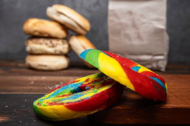 Gökkuşağı simit diliminin yakın görüntüsü ve tahtanın üzerinde kahverengi bir kese kağıdıyla çeşitli türde simit koleksiyonu.