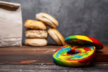 Gökkuşağı simit diliminin yakın görüntüsü ve tahtanın üzerinde kahverengi bir kese kağıdıyla çeşitli türde simit koleksiyonu.