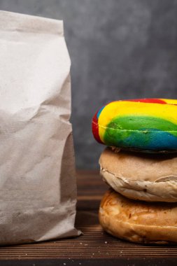 Muhtelif ekmeklerden oluşan bir yığın ve tahta bir tahtanın üzerinde kahverengi bir kese kağıdı.