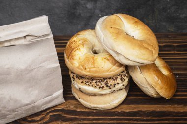 Muhtelif ekmeklerden oluşan bir yığın ve ahşap bir tahtanın üzerinde kahverengi bir kese kağıdı.