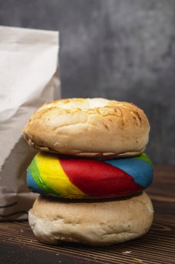 Muhtelif ekmeklerden oluşan bir yığın ve tahta bir tahtanın üzerinde kahverengi bir kese kağıdı.