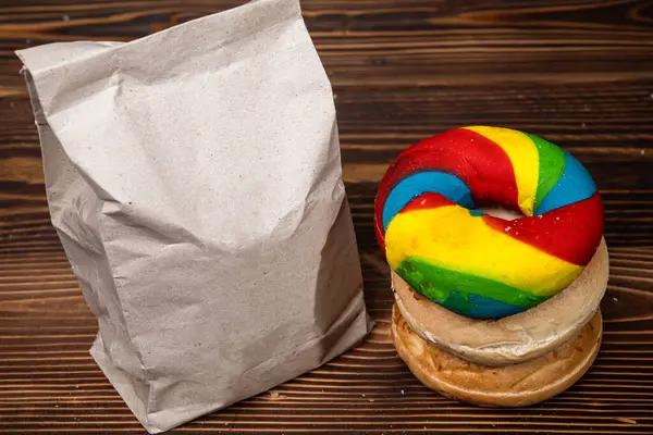 Muhtelif ekmeklerden oluşan bir yığın ve tahta bir tahtanın üzerinde kahverengi bir kese kağıdı.