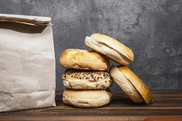 Muhtelif ekmeklerden oluşan bir yığın ve ahşap bir tahtanın üzerinde kahverengi bir kese kağıdı.