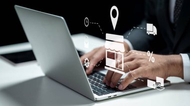 İşadamı ekommerce için bir dükkanın ikonunu gösterirken dizüstü bilgisayar kullanıyor. Tablet masanın üzerinde. Sanal ekranda teknolojik yenilik. Ekommerce ya da küçük işletme kavramı