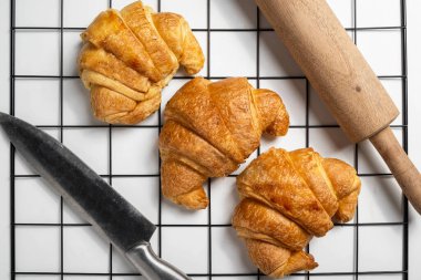 Soğutma tepsisinde taze kruvasan ve beyaz arka planı olan bir bıçak ve merdane. Üst görünüm