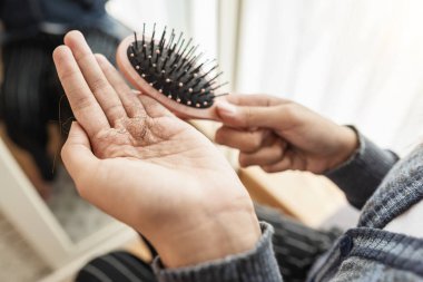 Yatak odasında saçını taradıktan sonra saç dökülme sorunu olan bir kadın. Kişisel bakım ve sağlık rutinleri kavramı