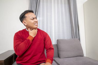 Endonezyalı güneydoğu Asyalı adam evdeki kanepede oturup öksürüyor. Astım ya da alerji krizinden muzdarip. Sağlık hizmetleri kavramı