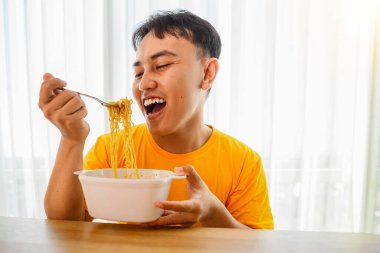 Endonezyalı güneydoğu Asyalı bir adam bir masada oturuyor ve lezzetli hazır erişteler yiyor.