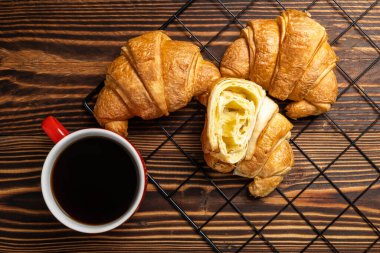 Soğutma tepsisinde taze pişmiş kruvasan ve ahşap arka planda bir fincan kahve. Üst görünüm