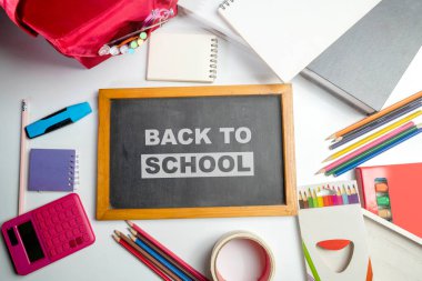 Sırt çantası ve okul gereçleri ile okula dönüş mesajı olan bir karatahtanın yakın görüntüsü. Okula Dönüş kavramı. Üst görünüm