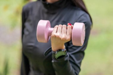 Spor kıyafetli bir kadın halka açık bir parkta dambılla pratik yapıyor. Sağlıklı aktif yaşam tarzı kavramı