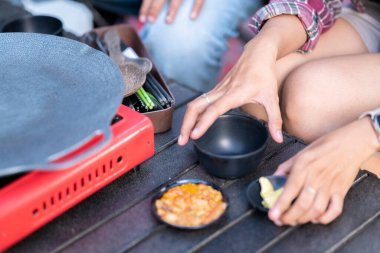 İnsanlar dışarıda yemek hazırlıyor, portatif bir soba ve çeşitli malzemeler sergiliyorlar. Doğal ortamdaki yemekten zevk alma sahnesi.