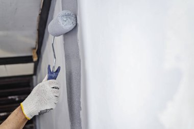 Ev tadilatı sırasında duvara boya sürmek için boya silindiri kullanan eldivenli inşaat işçisi. Ev yenileme projesi