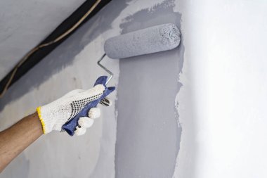 Ev tadilatı sırasında duvara boya sürmek için boya silindiri kullanan eldivenli inşaat işçisi. Ev yenileme projesi