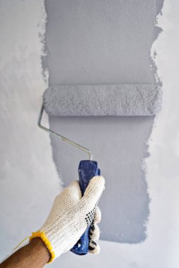 Ev tadilatı sırasında duvara boya sürmek için boya silindiri kullanan eldivenli inşaat işçisi. Ev yenileme projesi