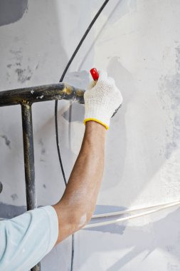 Ev tadilatı sırasında duvara boya sürmek için fırça kullanan eldivenli inşaat işçisi. Ev yenileme projesi