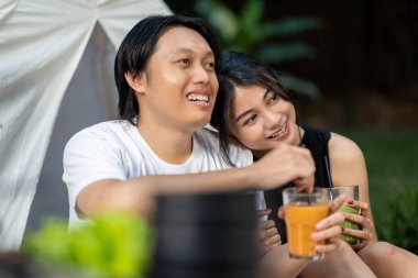 Endonezyalı güneydoğu Asyalı çift dışarıda otururken gülümsüyor ve serinletici içkilerin tadını çıkarıyor. Doğal ortamdaki yemekten zevk alma sahnesi.